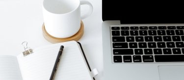 notebook and coffee cup next to laptop